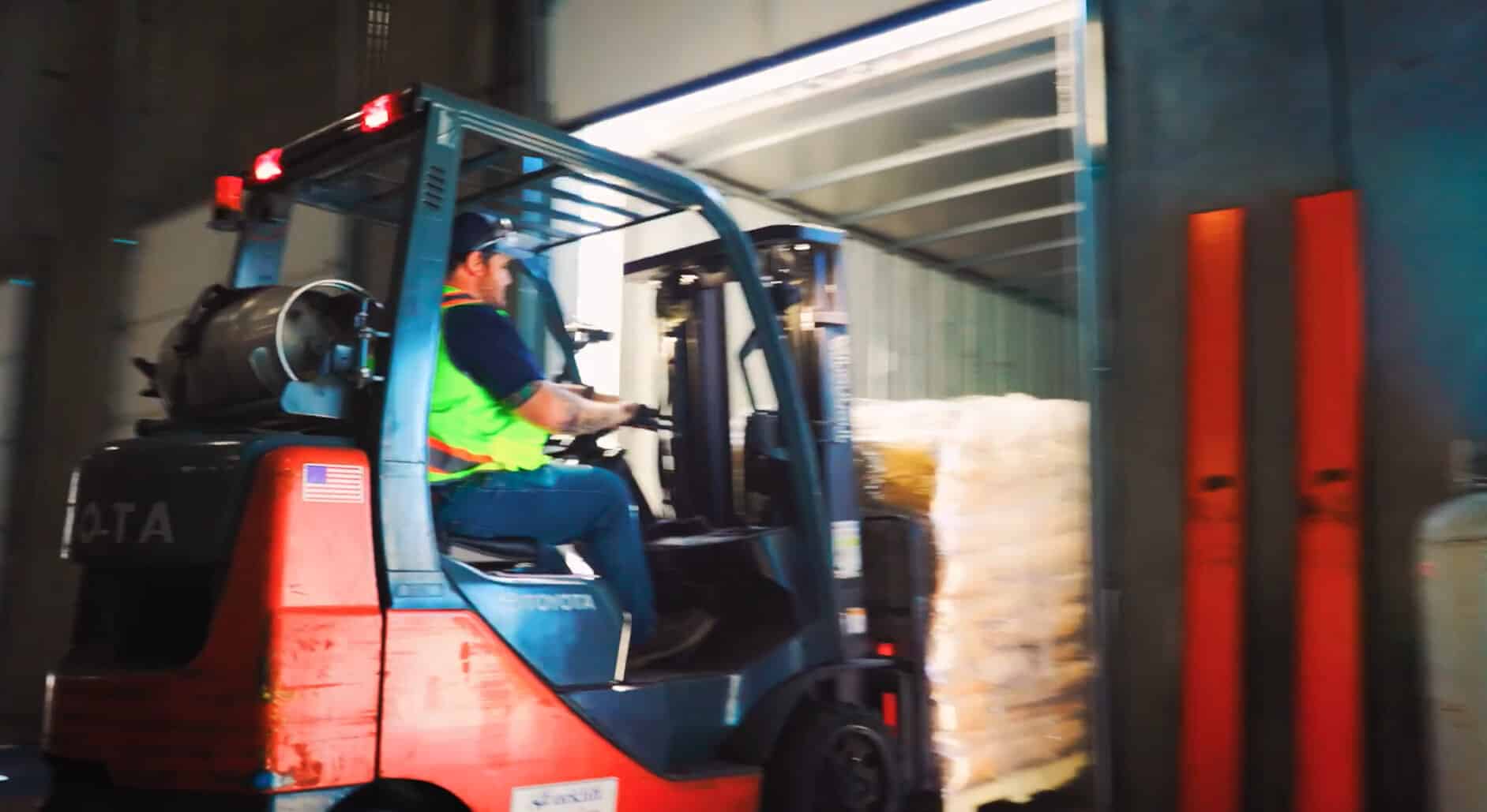 Person driving a skid loader moving merchandise inside a semi tractor trailer