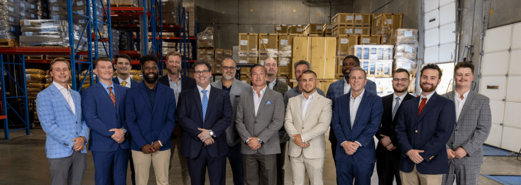 Men in suits and blazers posing in a warehouse with steel shelving and boxes